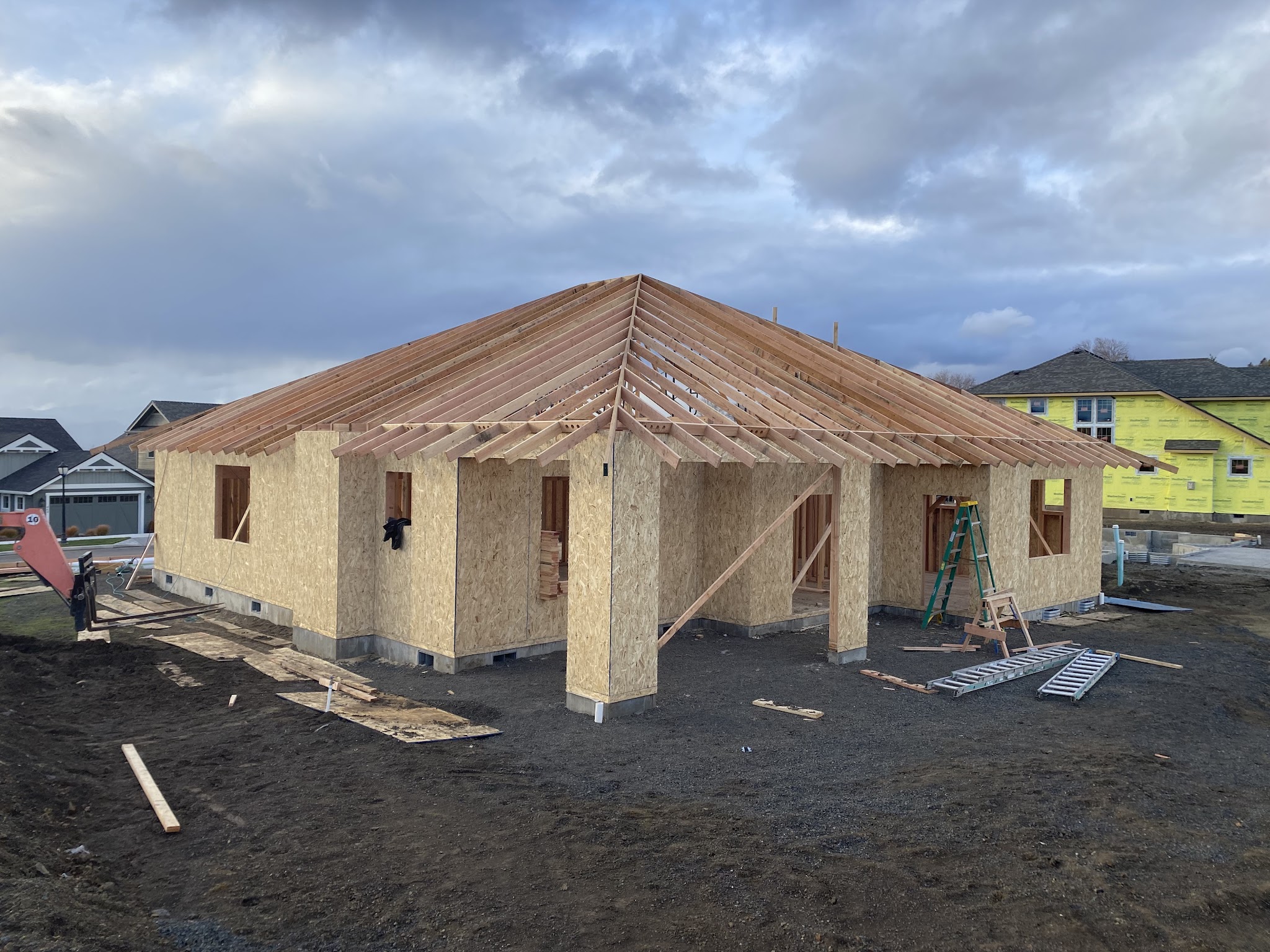 Framed house shell with OSB sheathing and roof trusses under an evening sky