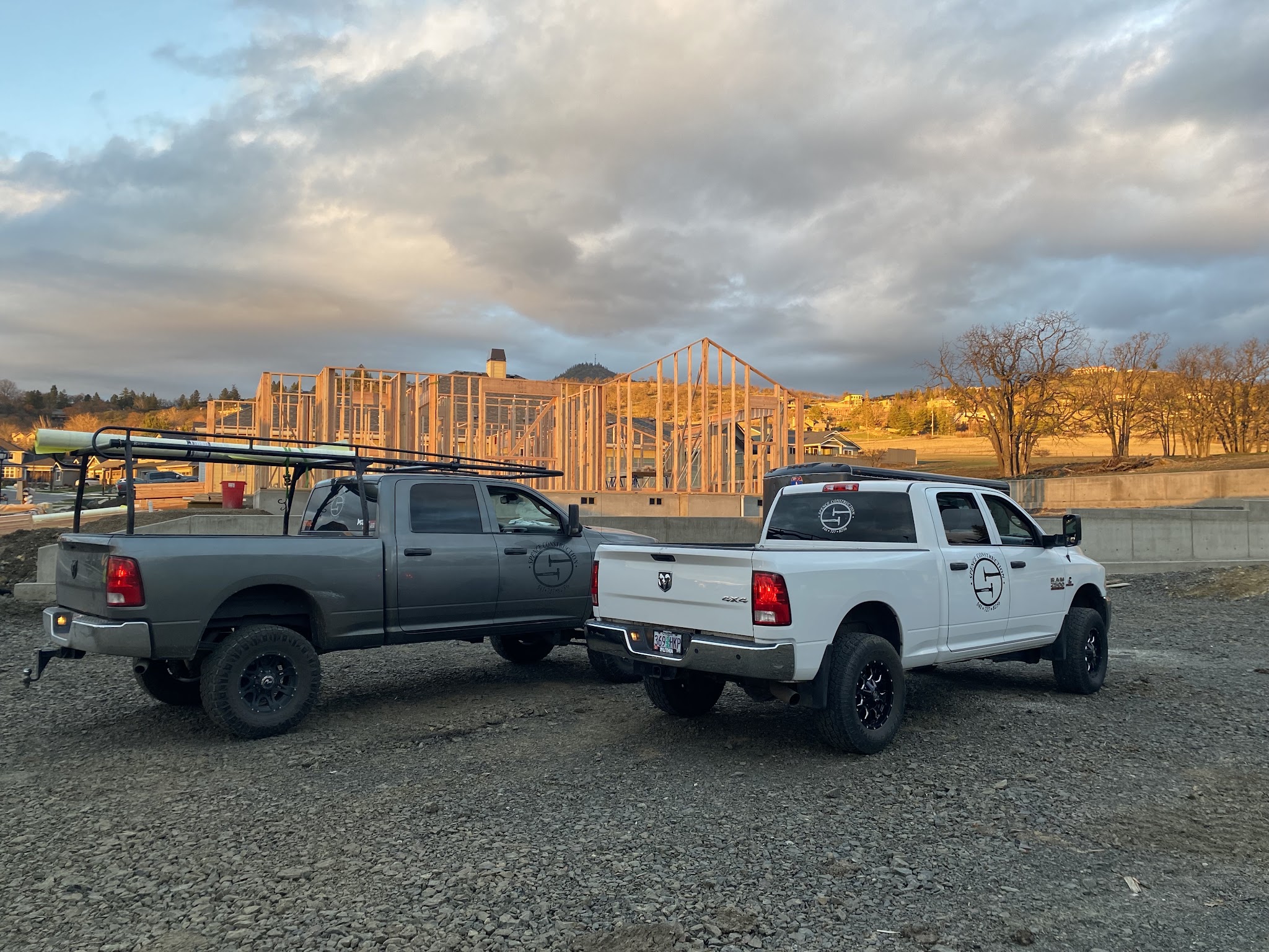 Two Spence Construction work trucks with the company's crossed-hammer logo, parked at a framed job site at golden hour