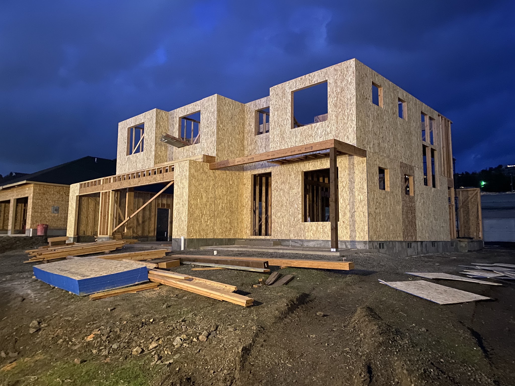 Two-story home framed with OSB sheathing at night, ready for siding