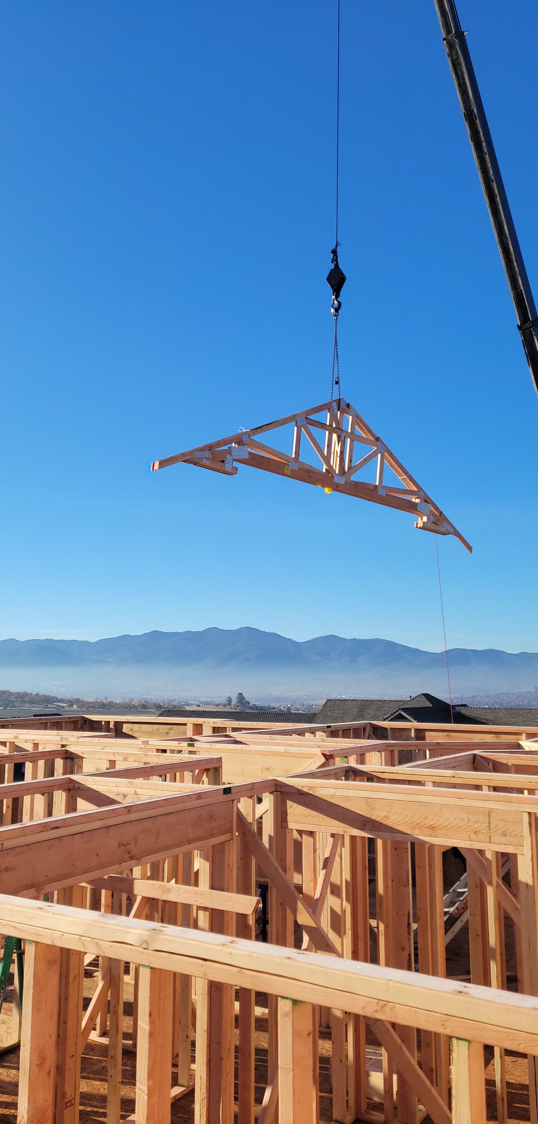 Crane lifting a roof truss into place on a Spence Construction job site, Rogue Valley mountains in the background